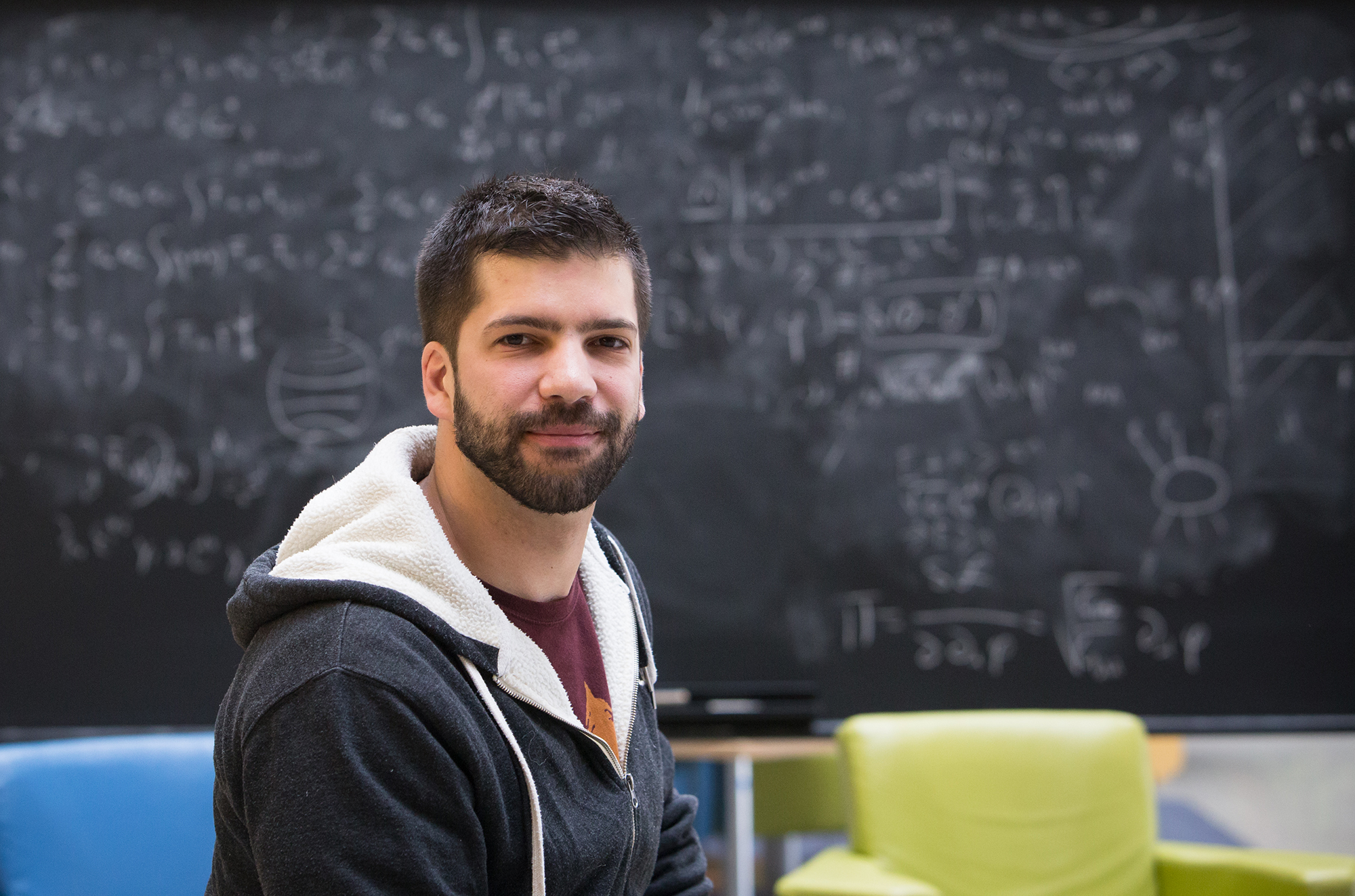 Giacomo Torlai stands in front of a blurry blackboard filled with equations in PI's atrium