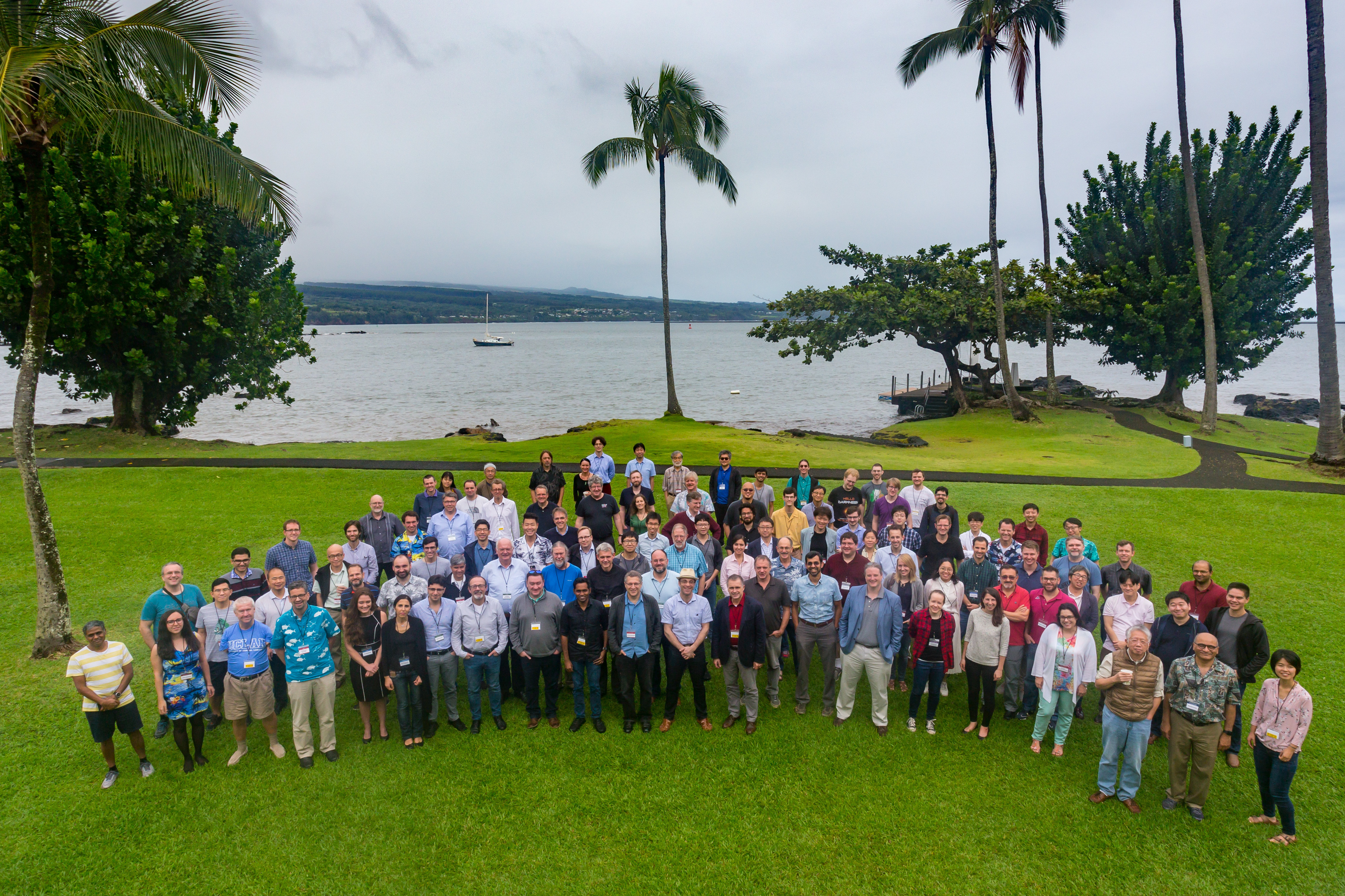 Un grand rassemblement de membres de la collaboration EHT sur la pelouse avec des palmiers et un fond océanique.
