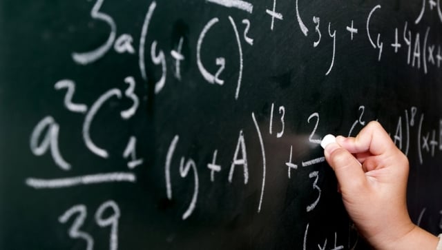 Picture of a hand writing equations on a blackboard