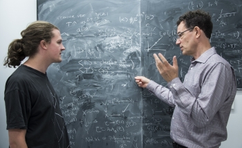 Steffen Gielen and Neil Turok interacting in front of a blackboard covered in equations and graphs