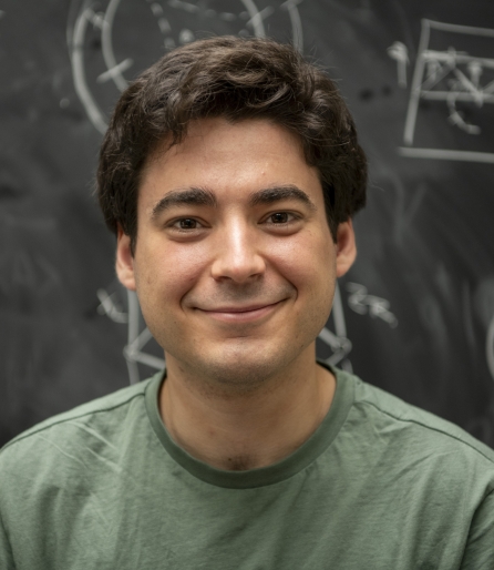 Portrait of a young man wearing a green shirt in front of a blackboard of equations